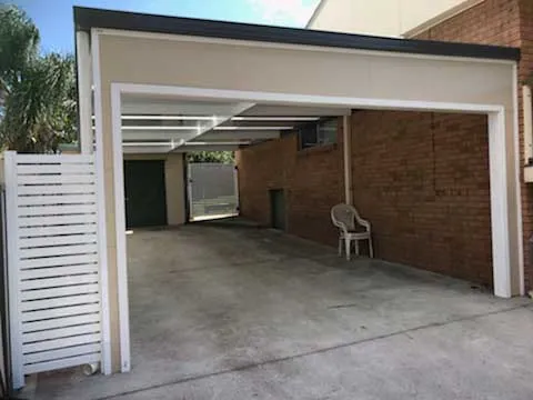 A stylish, modern home with a large, dark grey fixed awning providing shade over a patio area, featuring outdoor furniture.